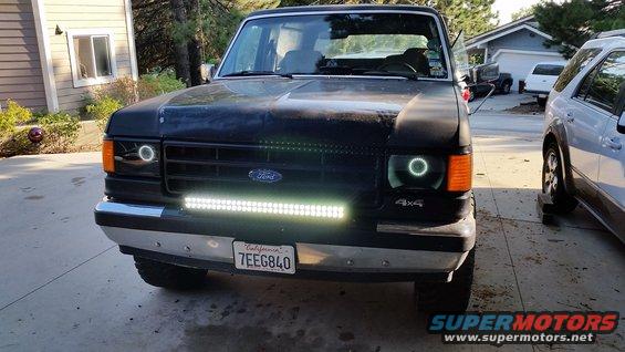 Black Ford truck with aftermarket halo headlights and a light bar, front view