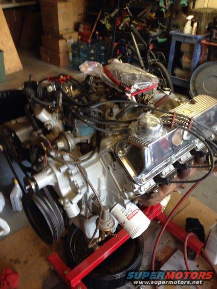 V8 engine on a red stand, with chrome valve covers and an oil filter. It's in a garage with boxes and a bike in the background