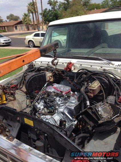 White vehicle engine bay with engine hoist lifting a chrome-accented engine