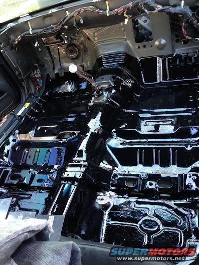Car interior floor pan with black coating, exposed wiring, and part of a gear shifter