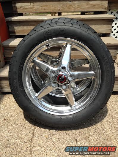 Chrome 5-spoke wheel with a tire, sitting on concrete in front of wooden steps