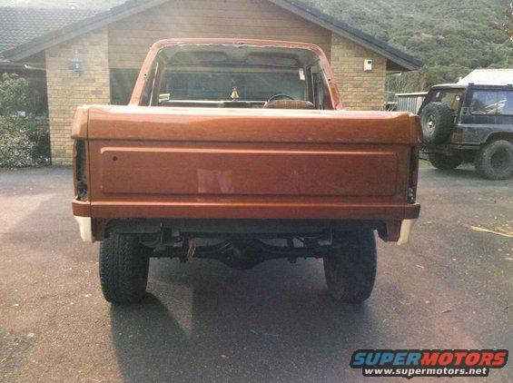 Rear view of an orange pickup truck with its tailgate down, parked outside a house. Another SUV is visible to the right