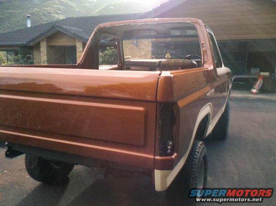Brown 1980s Ford Bronco with white trim, rear 3/4 view, showing damage to the roofline