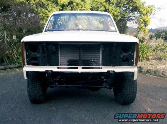 White truck front end, missing grille and headlights. Visible radiator. Tires are large