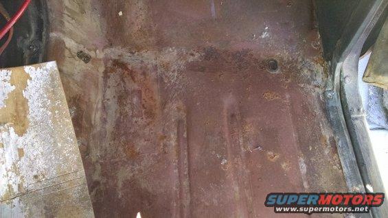 Close-up of heavily rusted floor pan with some peeling paint and wiring