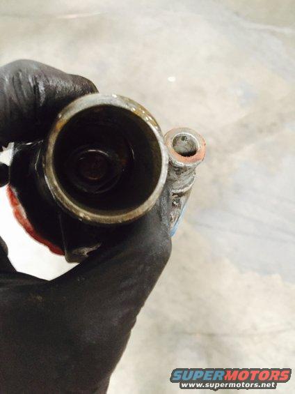 Gloved hand holding a dirty, worn metal cylinder with a smaller tube attached