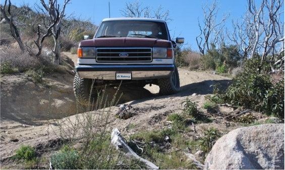 Maroon and white Ford Bronco on a dirt trail, front view. License plate is visible