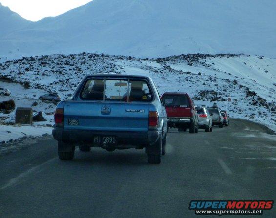 Blue pickup truck in a line of vehicles on a snowy mountain road