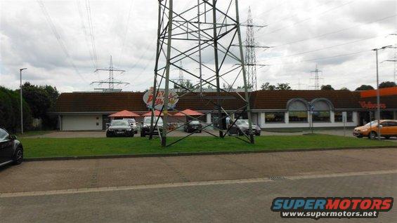 Several cars parked in front of a building, with a large power line tower dominating the foreground