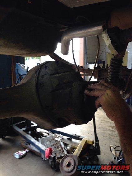 Rear differential assembly with exhaust pipe and a hand touching it, under a vehicle