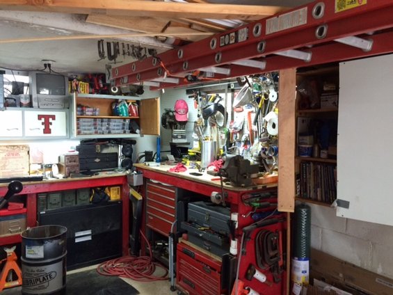 Workshop with tool chests, workbench, tools hanging on wall, and ladders overhead
