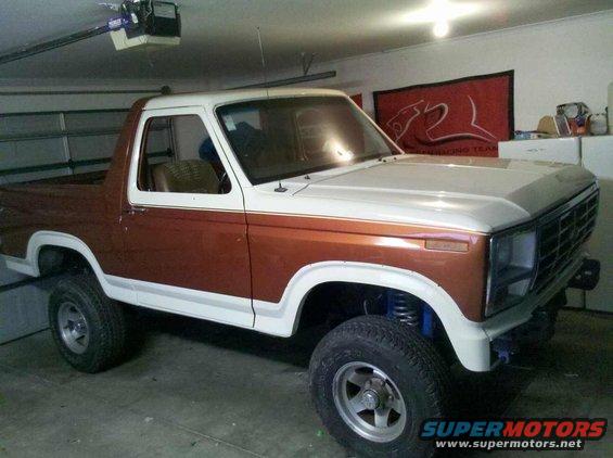 Two-tone brown and white Ford Bronco with aftermarket wheels and suspension, parked indoors