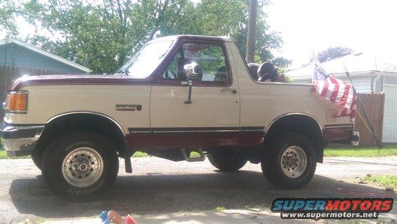 1988 Ford Bronco parked in driveway, side view, American flag on rear