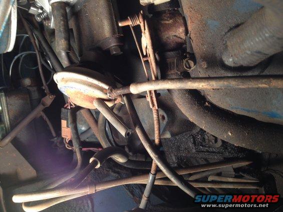 Engine bay with hoses, cables, and rusty metal parts. A blue painted surface is visible