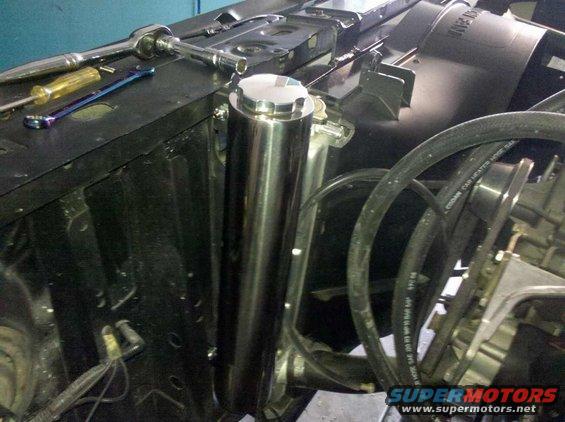 Engine bay with a chrome overflow tank, tools, and hoses. Some text is visible on a hose
