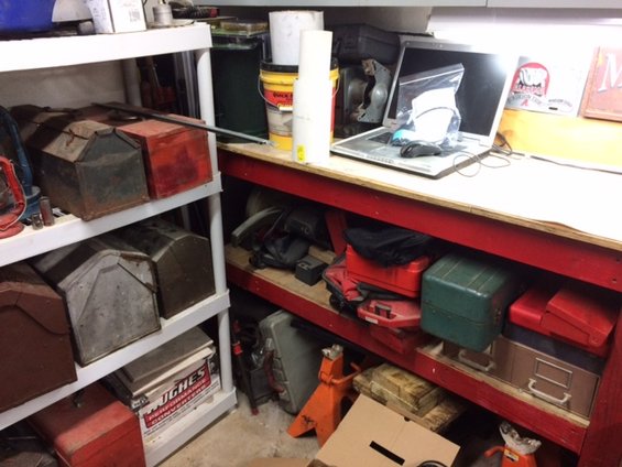 Shelves filled with toolboxes, paint cans, and a laptop on a workbench