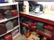 2004 Aston Martin Virage - A cluttered workshop scene with storage shelves holding various tools and equipment, including a laptop on the workbench.