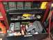 2004 Aston Martin Virage - A red and black toolbox is filled with various tools, including grinders, drills, and other hardware, with ammo cans stored above.
