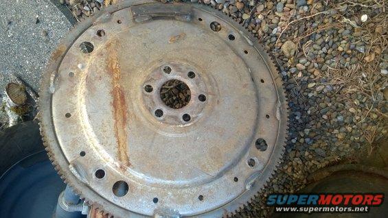 Rusty metal flywheel with a ring of teeth and bolt holes, lying on gravel