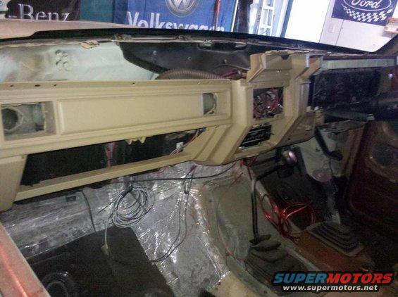 Tan dashboard and floor of a disassembled vehicle, showing exposed wiring and insulation