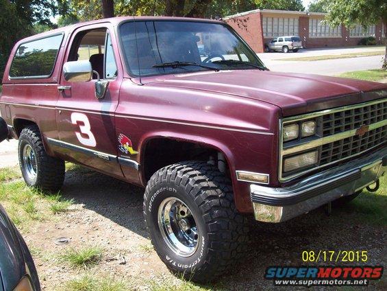 Maroon SUV with racing stripe and number 3 on the door. It has large off-road tires and chrome wheels