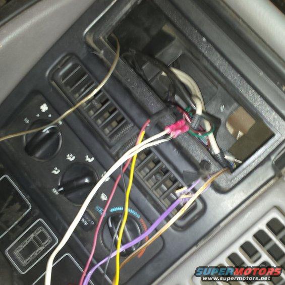 Car dashboard with exposed wires and connectors, showing air vents and control knobs