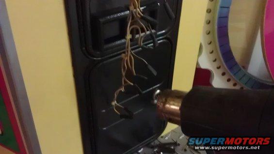 heat gun pointed at exposed wires on a black panel, with a colorful circular object in background