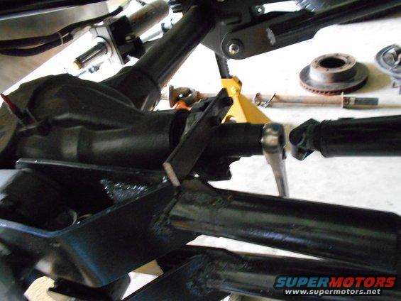 Vehicle suspension parts, including a differential, driveshaft, and brake rotor, on a yellow jack