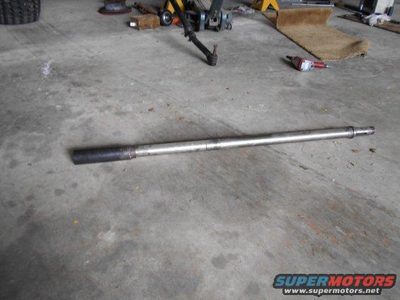 metal shaft with a black end and a flanged end, lying on a concrete floor
