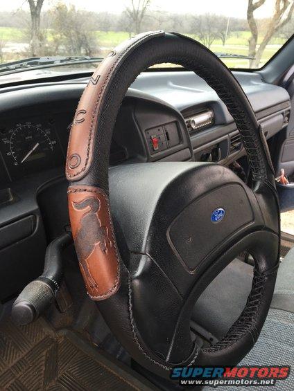 Interior shot of a 1993 Ford Bronco showing the steering wheel with a custom leather cover a Bronco emblem and the word 'BRONCO' stitched on it