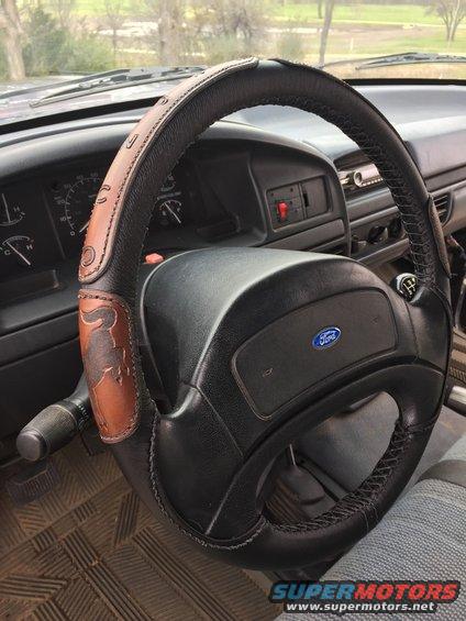 Black steering wheel with brown leather cover a bull graphic, Ford logo on airbag cover