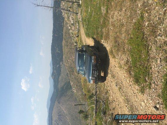 Dark blue SUV on a dirt road with mountains in the background. The vehicle has a snorkel and off-road tires