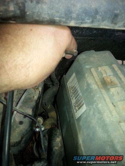 Hand adjusting a metal rod near a gray electrical box with a barcode
