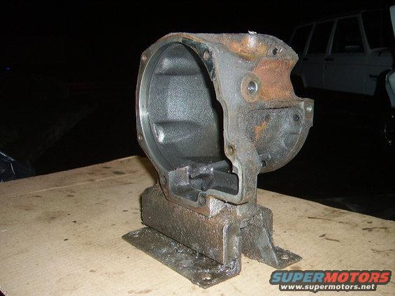 Cast iron differential housing part on a workbench. A white vehicle is visible in the background