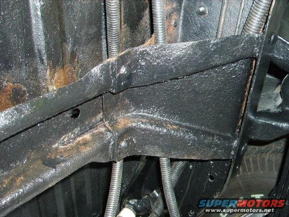 Underside of a vehicle showing frame rails, suspension parts, and some rust