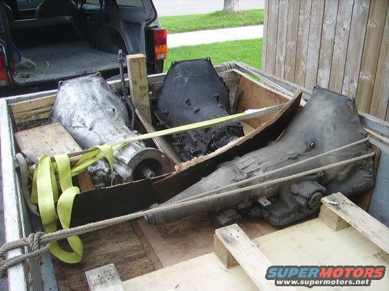 three transmissions loaded in a truck bed, one silver, two black, secured with straps and rope