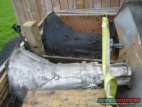 Two transmissions, one black and one silver, secured with yellow straps in a wooden crate