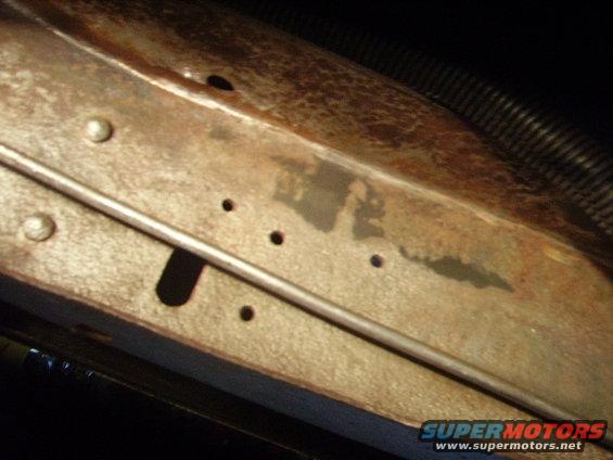 Close-up of rusted metal frame showing rivets, small holes, and a metal rod