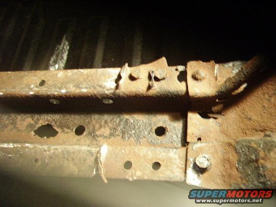 Rusted metal frame with bolts and holes, showing significant corrosion