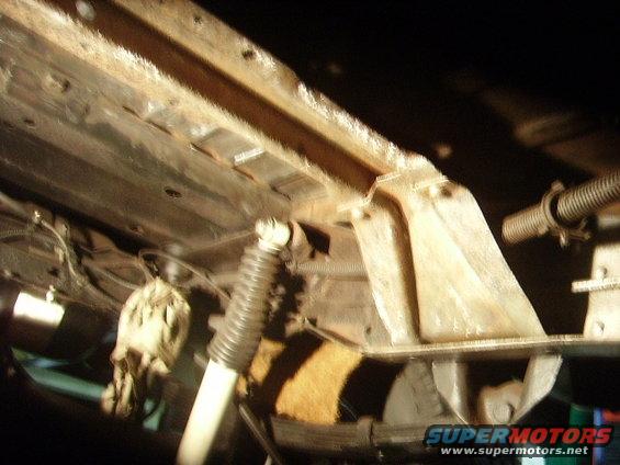 Underside of a vehicle showing rusty frame rails, a shock absorber, and suspension components