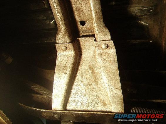Rusted metal bracket with visible bolts and a ribbed hose underneath