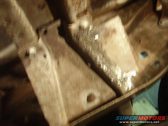Underside of a vehicle showing frame rails and suspension parts. Some areas appear to have been welded