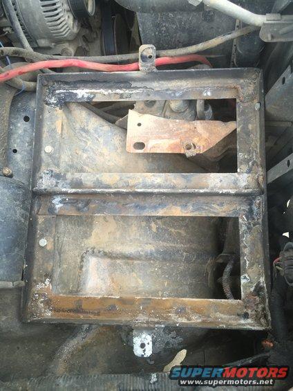 Close-up of a rusty, empty battery tray in an engine bay