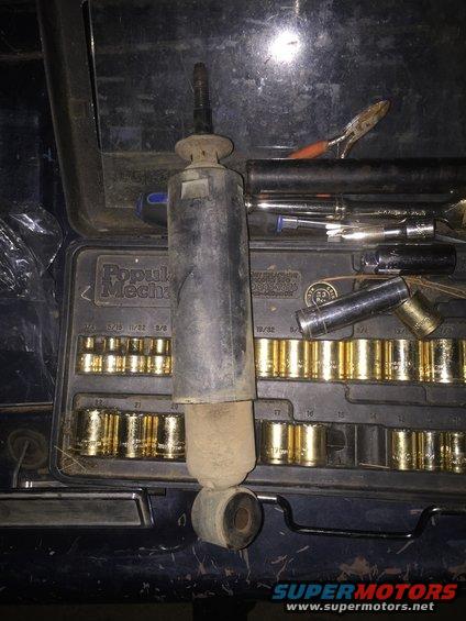Shock absorber sitting on top of a Popular Mechanics socket set. Pliers and other tools are also visible
