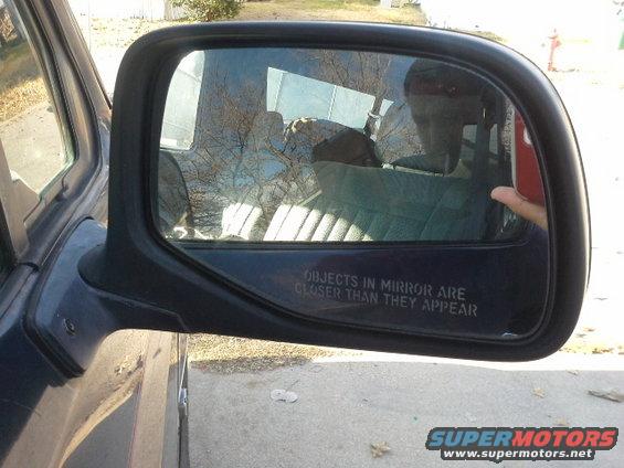 Side mirror showing interior with striped seats and reflection of trees and a person