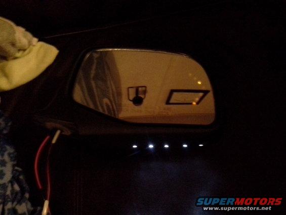 Side mirror showing reflections of a camera icon and a rectangular indicator light