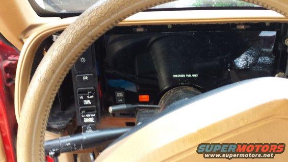 Dashboard view of a car interior, showing steering wheel, dashboard controls, and part of the instrument cluster. Text on the steering column reads 'UNLEADED FUEL ONLY'