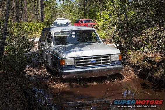 Ford Bronco driving through a muddy trail with other vehicles behind it