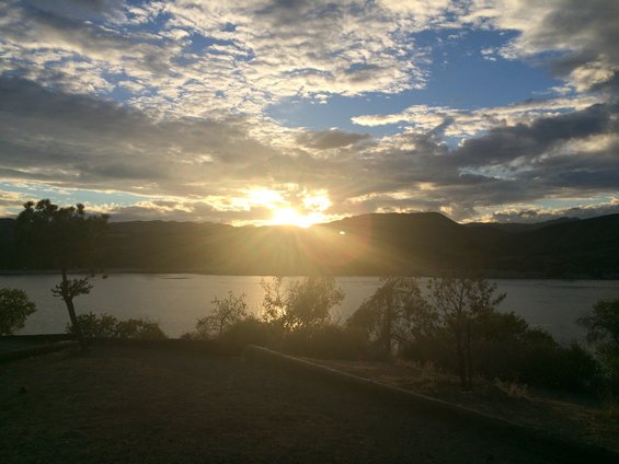 Sunset over a calm lake, with silhouetted mountains and trees in the foreground