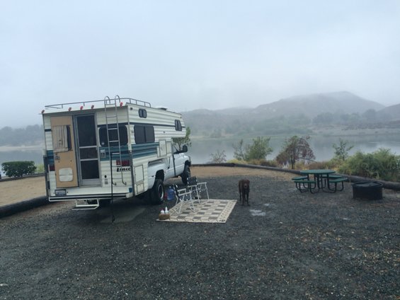 Motorhome on a white truck chassis, rear view, parked at a campsite by a lake